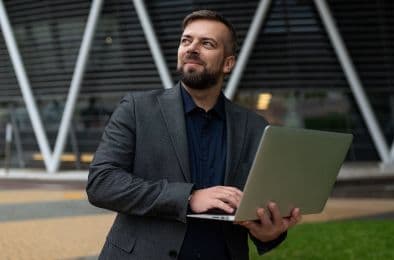 A picture of a man walking and holding his laptop, looking in a different direction.