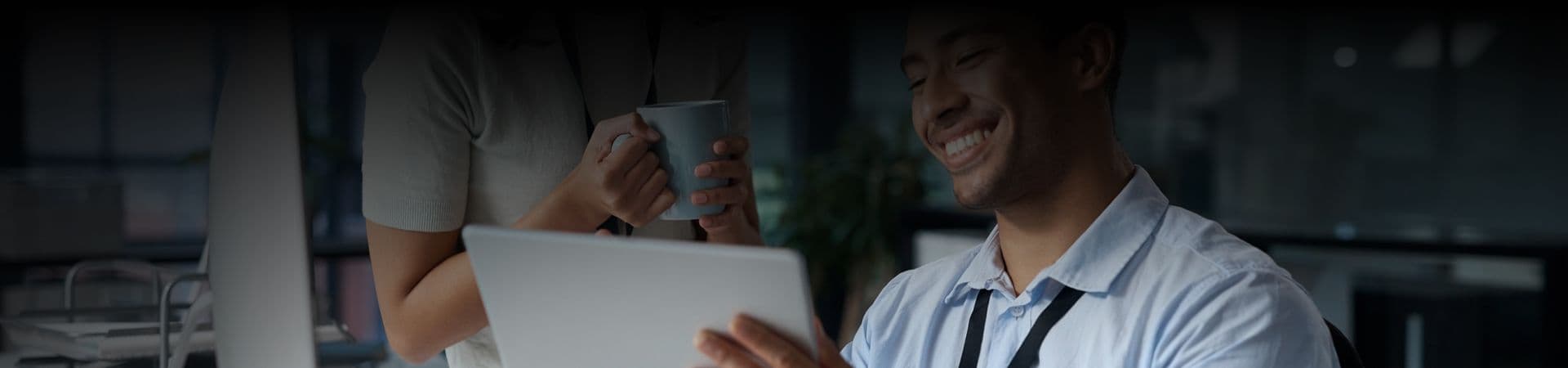 A picture of a man showing something on his tablet to a woman, and both of them sharing a laugh.